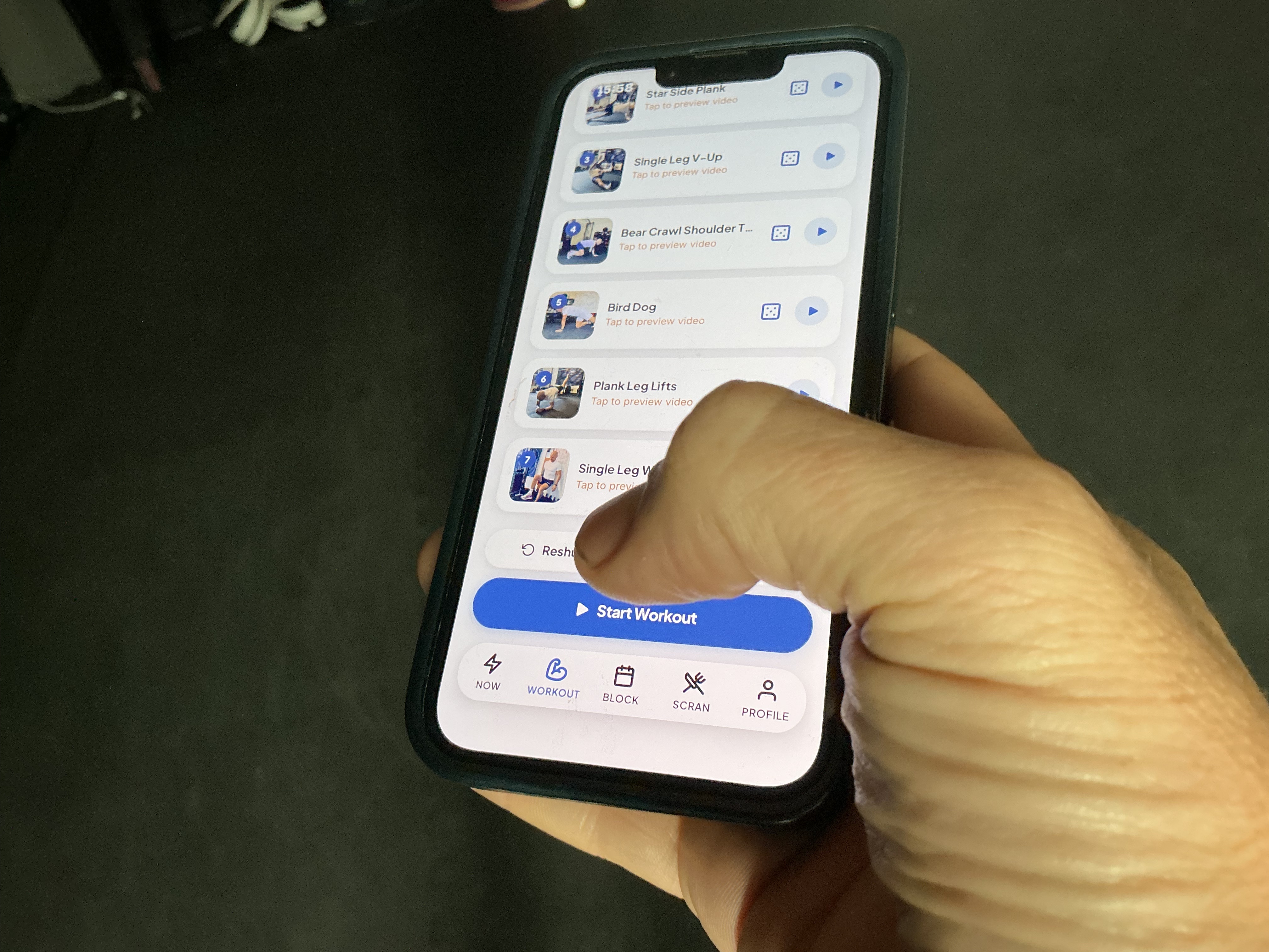 A hand holding a phone showing a Core Buddy workout — a list of exercises with video previews and a start workout button