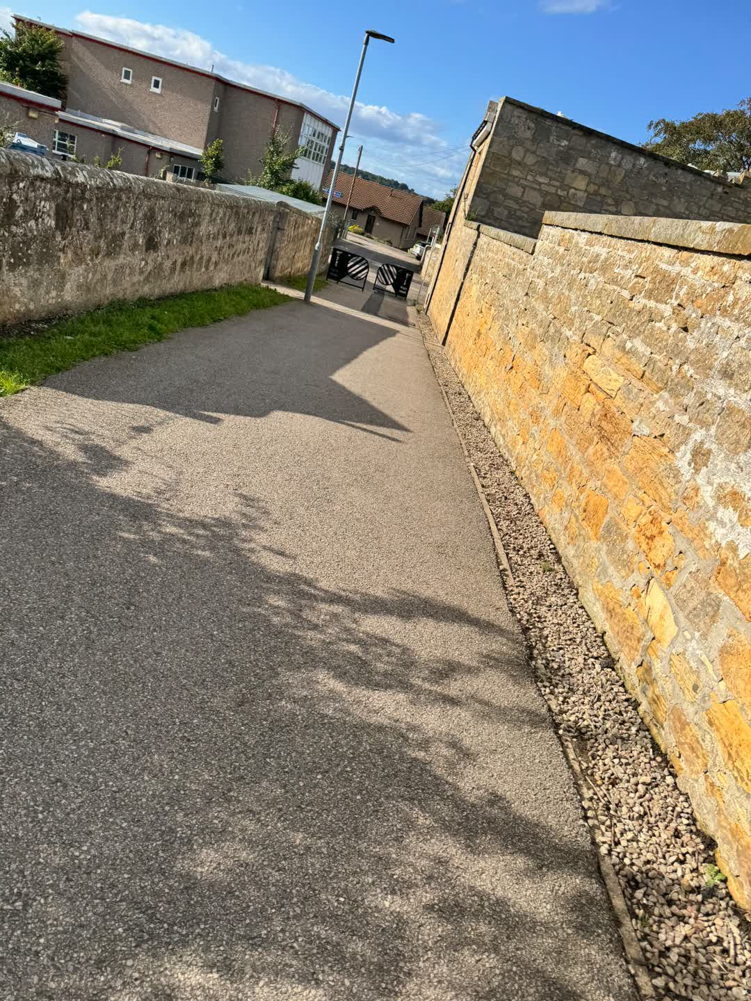 The lane Gillian walks, stone walls either side on a bright afternoon
