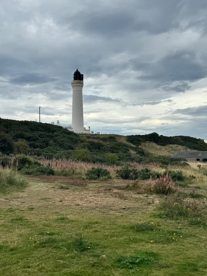 Covesea lighthouse on the headland above the shore, under a grey sky