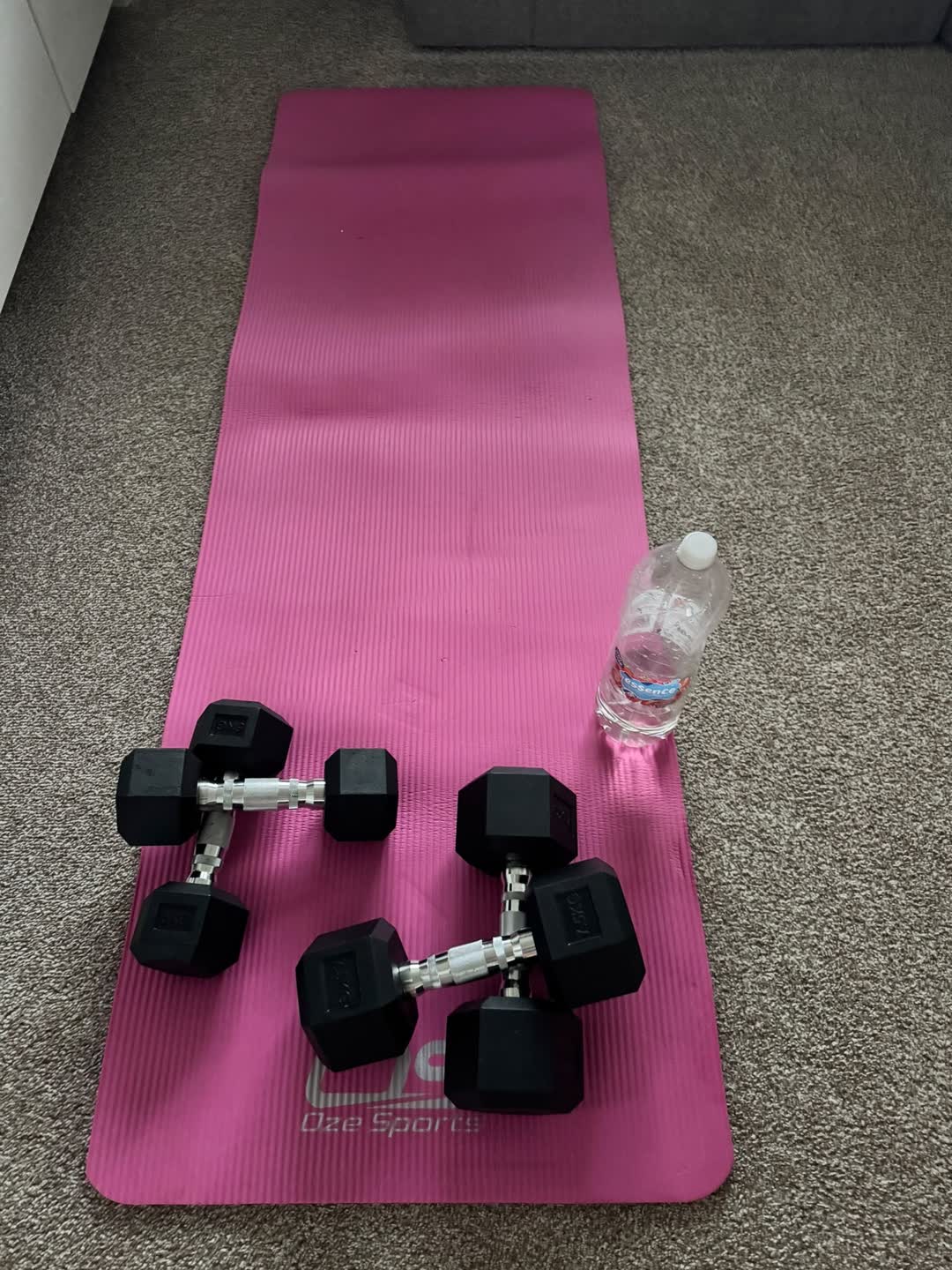 A pink exercise mat laid out with two pairs of dumbbells and a water bottle
