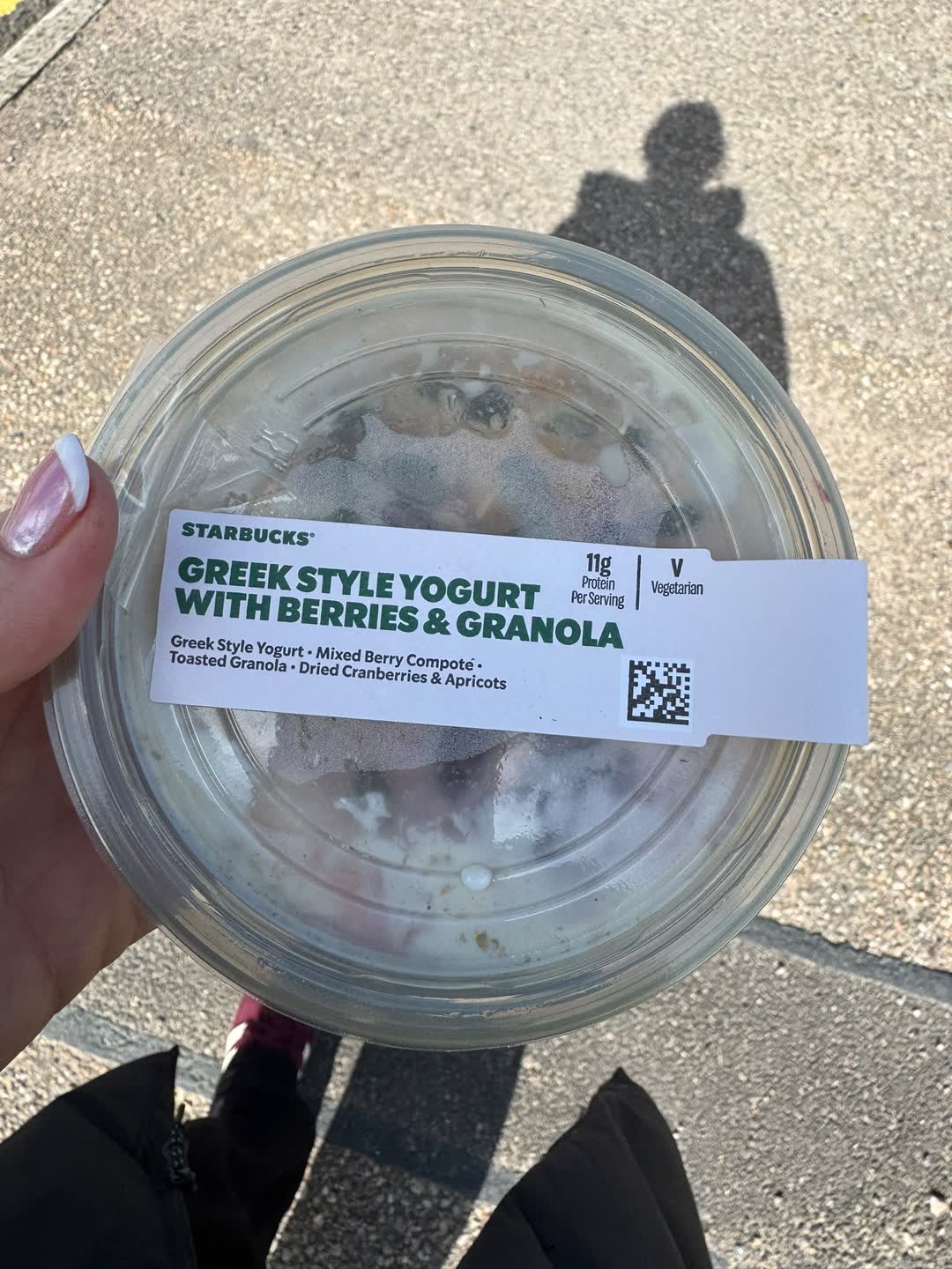 A pot of Greek style yogurt with berries and granola held up outdoors