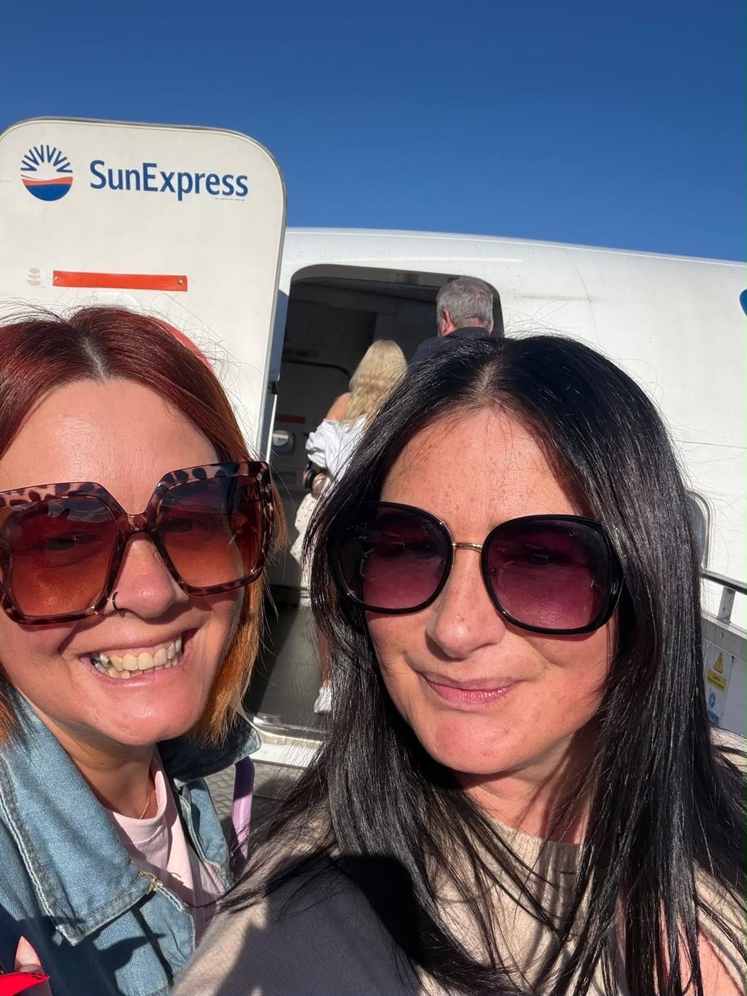 Sarah and a friend in sunglasses, smiling at the foot of the aircraft steps