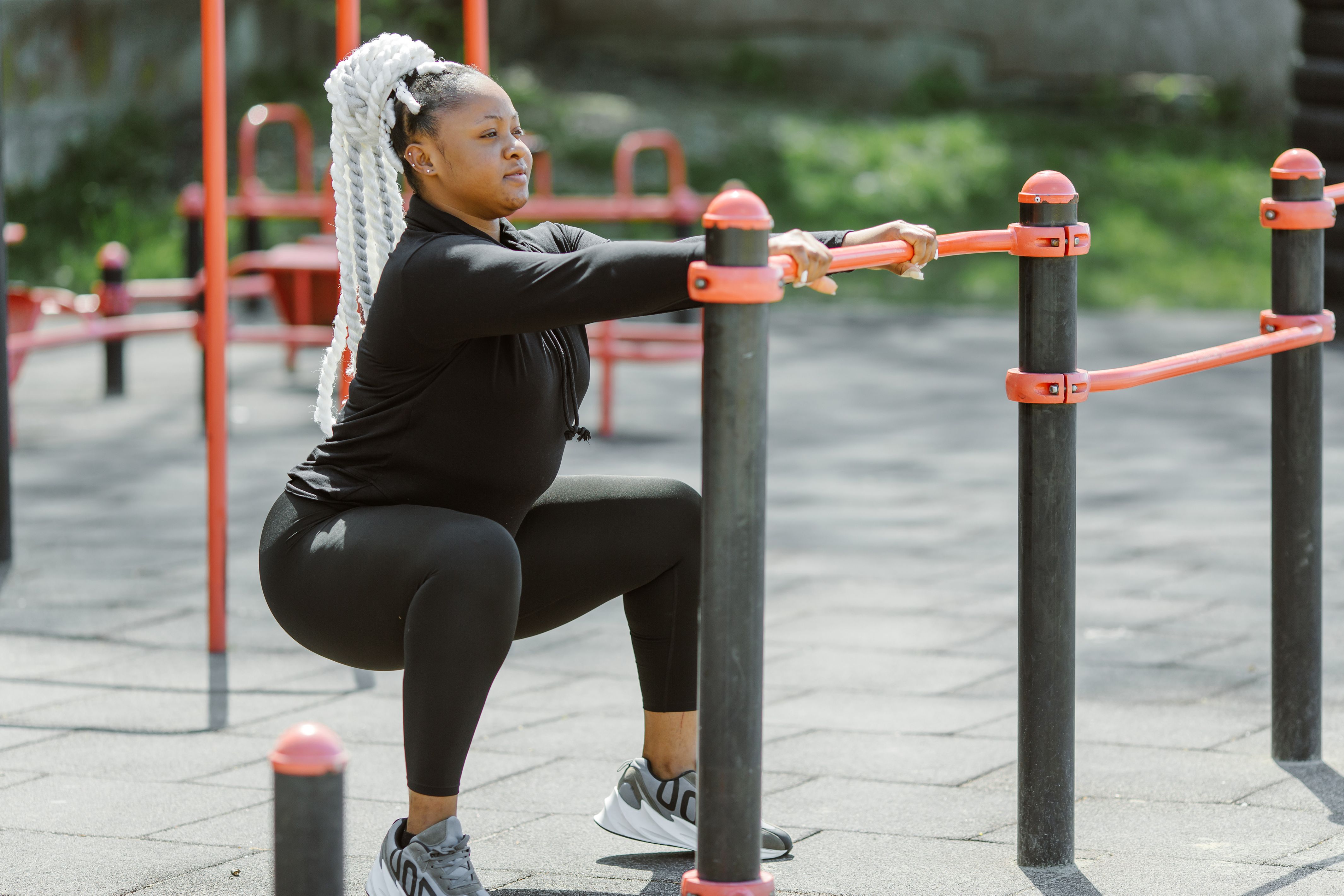 A woman doing a supported squat holding a rail at an outdoor exercise area
